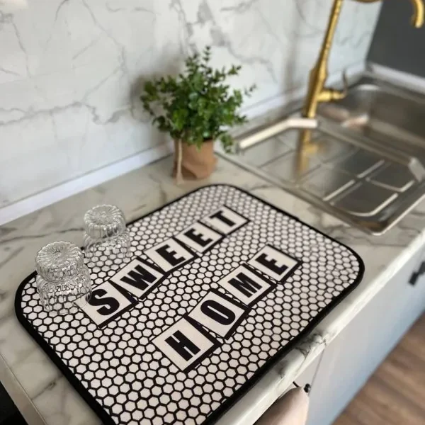 Alt: نم‌گیر آشپزخانه طرح Sweet Home با زمینه مشبک سفید مشکی روی کابینت مرمری همراه با لیوان‌های شیشه‌ای