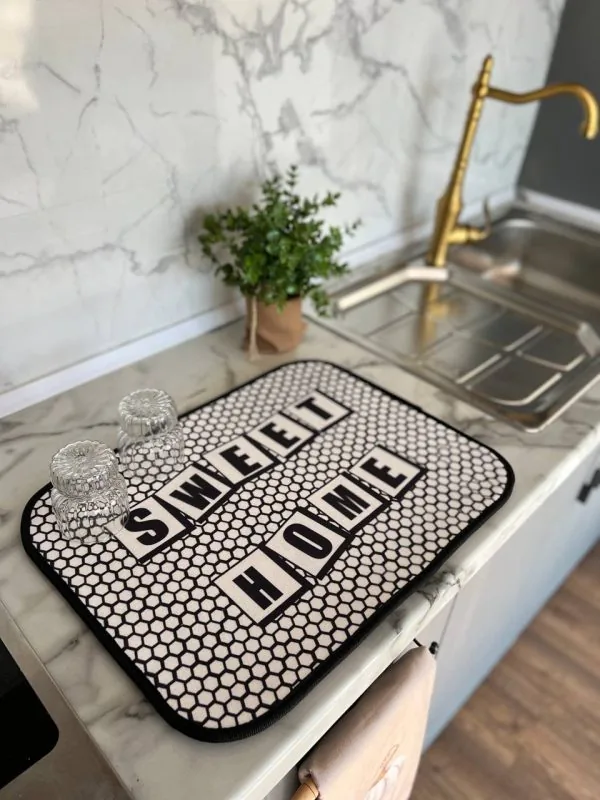 Alt: نم‌گیر آشپزخانه طرح Sweet Home با زمینه مشبک سفید مشکی روی کابینت مرمری همراه با لیوان‌های شیشه‌ای