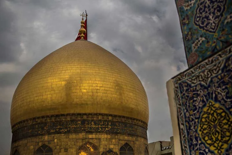 تصویر گنبد طلایی با پرچم قرمز و آسمان ابری در پس‌زمینه